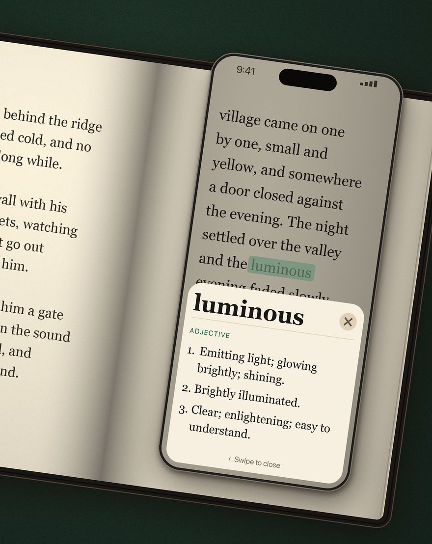 An iPhone held over an open novel; the word luminous is highlighted on the page and its dictionary definition is shown below it.